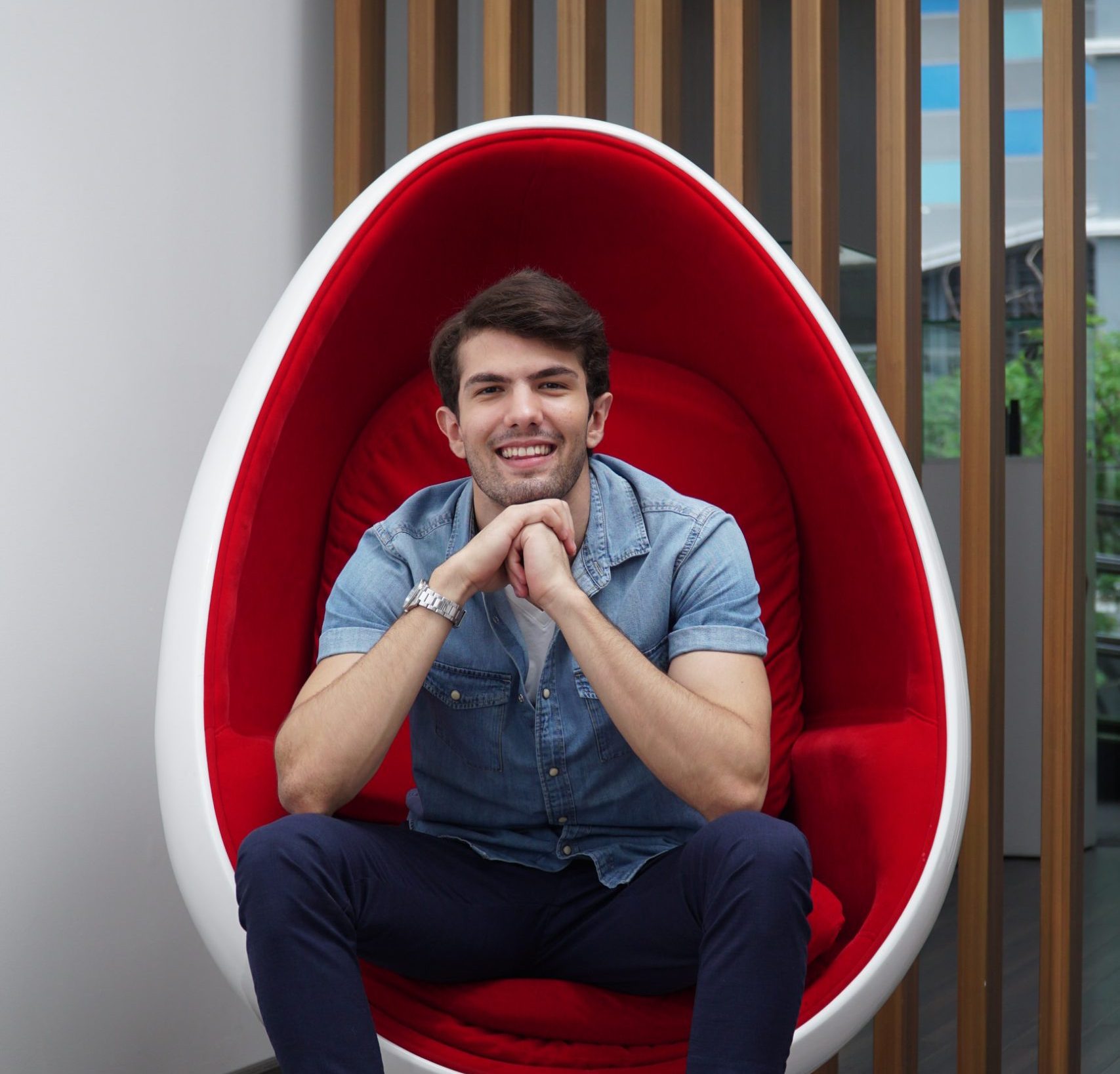 A man smiling after LED teeth whitening at The Smile Bar Philippines, sitting in a red egg chair.
