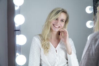 Woman smiling after LED teeth whitening session at The Smile Bar Philippines, showing bright natural teeth in front of a mirror with lights.