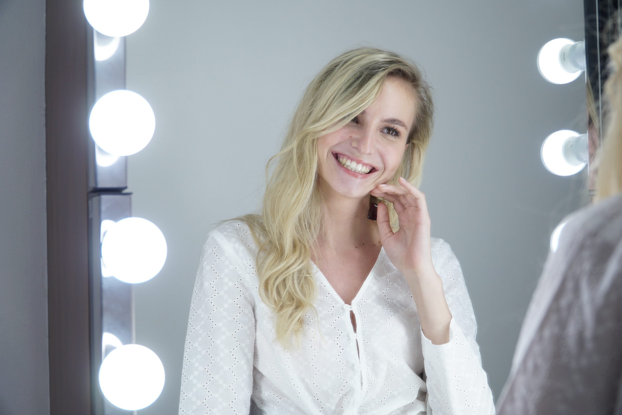 Woman smiling after LED teeth whitening session at The Smile Bar Philippines, showing bright natural teeth in front of a mirror with lights.